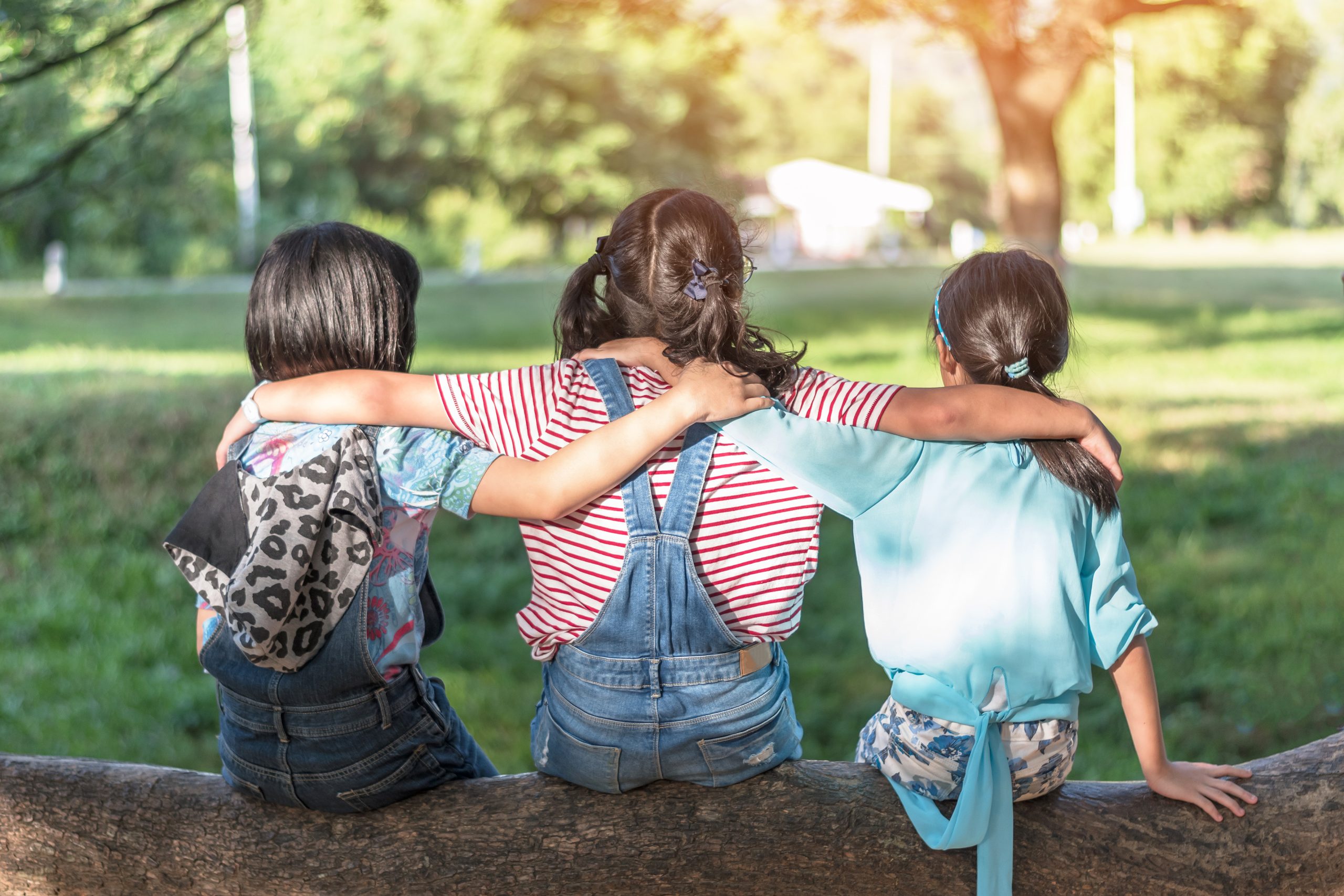 Children friendship concept with happy girl kids in the park having fun sitting under tree shade